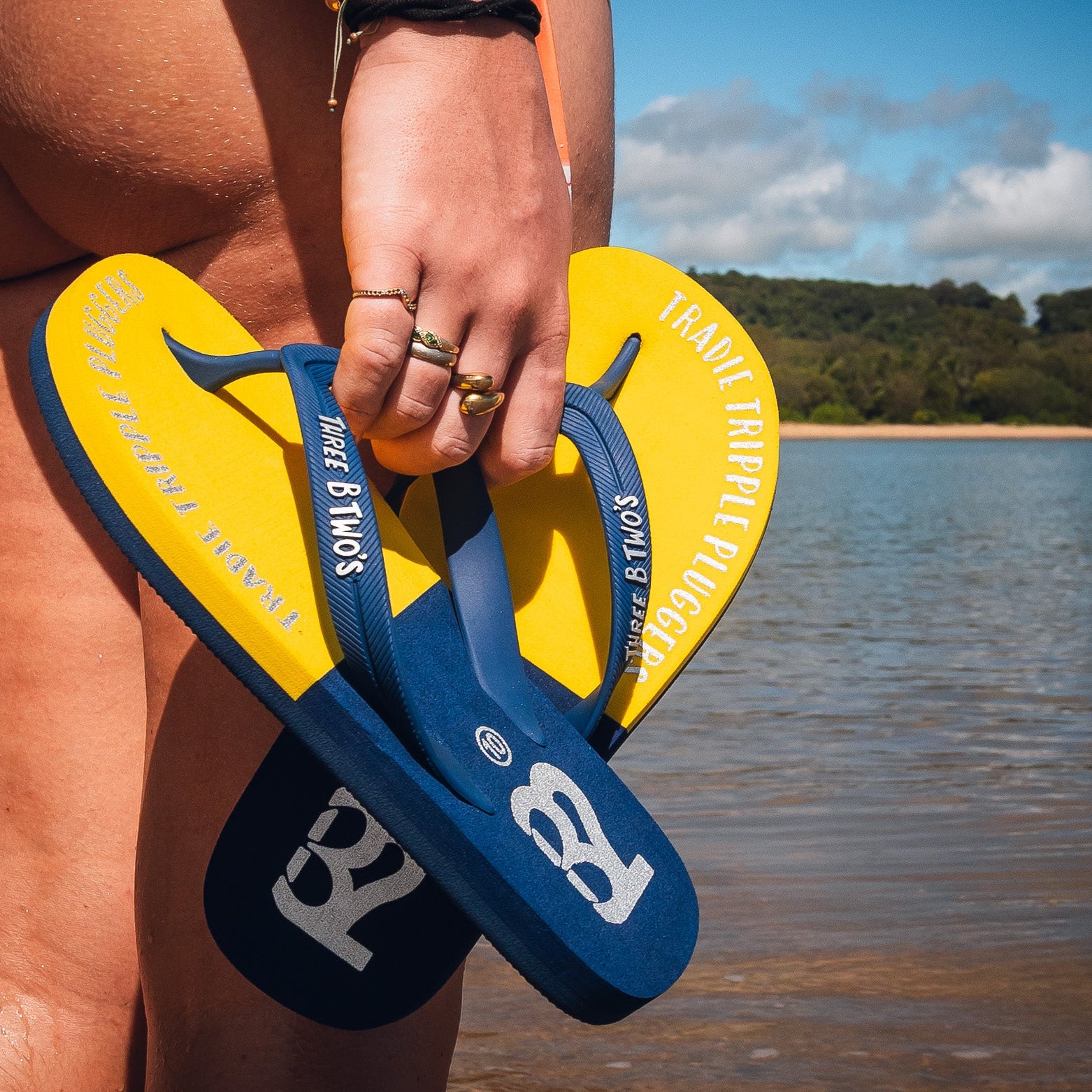 Person holding blue and yellow flip-flops with a beach background