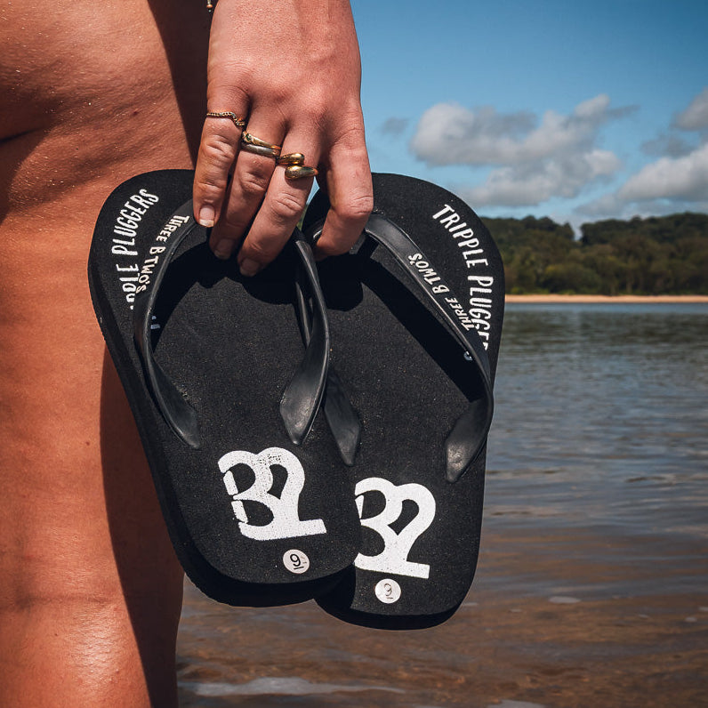 Person holding black flip-flops with a beach and water background